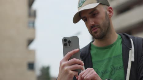 Serious-young-man-holds-a-smartphone-and-takes-a-photo-outdoors-in-city