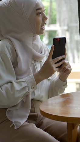 An-upwardly-mobile-Asian-Muslim-woman-enjoying-a-relaxing-moment-in-the-coffee-shop-on-a-bright-sunny-day