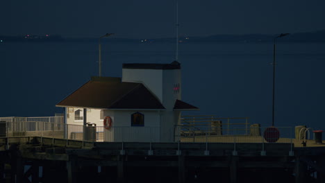 Pier-Und-Kabine-Im-Abendlicht,-Mit-Wasser-Und-Entfernten-Blinkenden-Lichtern-Dahinter,-Statisch