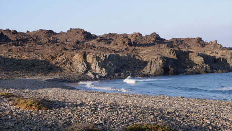 Panning:-Ocean-waves-wash-ashore-on-rugged-rocky-beach,-sunny-morning