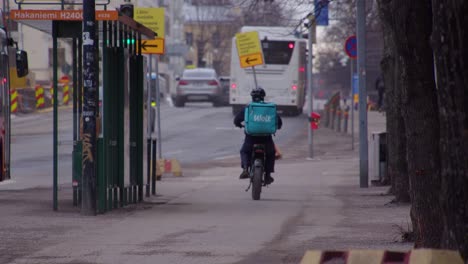 Food-delivery-rider-on-electric-bike-rides-on-sidewalk-of-city-street
