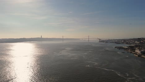 Panorámica-Aérea-Del-Mediodía-Del-Río-Tajo-Y-El-Puente-Colgante-Que-Conecta-Lisboa-Portugal