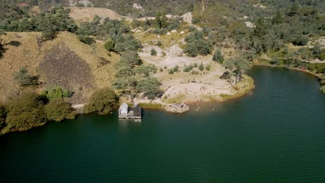 Reverse-aerial-of-Derby-Lake-Floating-Sauna-with-tourists-swimming-at-beach,-in-Derby,-Tasmania,-Australia