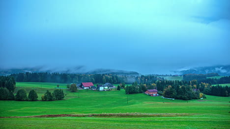 Pequeño-Pueblo-En-Los-Alpes-Con-Espesa-Niebla-Fluyendo-Arriba,-Vista-De-Lapso-De-Tiempo