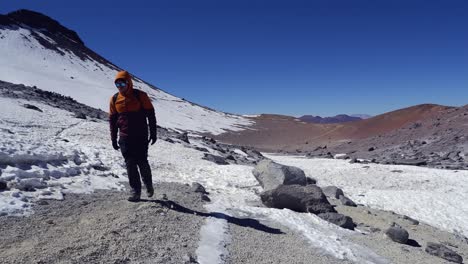 Hombre-Camina-En-Un-Día-Fresco-Y-Fresco-En-Una-Meseta-Montañosa-De-Grava-Nevada-En-Chile