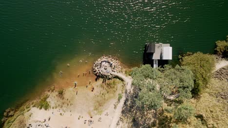 Drone-view-of-Derby-Lake-floating-sauna-and-tourists-swimming-in-fresh-water,-in-Derby,-Tasmania,-Australia