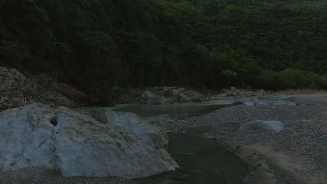 Drone-flying-at-low-altitude-over-dry-surface-of-Muchas-Aguas-river,-San-Cristobal-in-Dominican-Republic