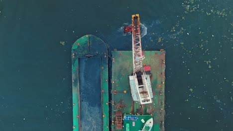 Top-down-aerial-over-dredging-operation-in-river-with-revolving-crane-and-barge