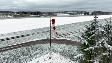 Drone-shot-from-a-small-snow-covered-airfield,-flying-past-the-red-and-white-windsock