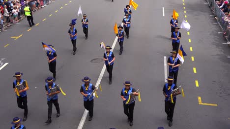 Estudiantes-De-La-Banda-De-Música-De-Mackay-North-State-High-School-Actuando-Y-Caminando-Por-La-Calle-Durante-El-Desfile-Del-Día-De-Anzac,-Honrando-La-Memoria-De-Aquellos-Que-Sirvieron-Y-Sacrificaron,-Vista-Superior.