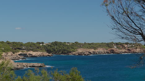 Wide-shot-of-Cala-Mondrago,-Mallorca,-with-crystal-clear-waters-and-waves-crashing-in-the-distance