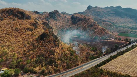 Aerial-view-of-road-and-mountains-in-Sangklaburi,-Thailand,-with-wildfires-casting-an-ominous-glow