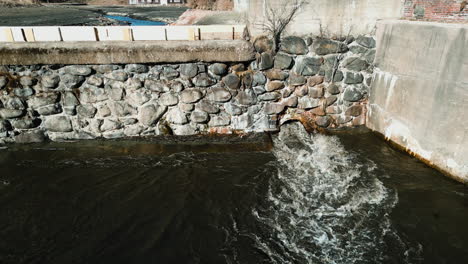 Drainage-outlet-with-heavy-flowing-water-at-base-of-dam,-aerial-establishing