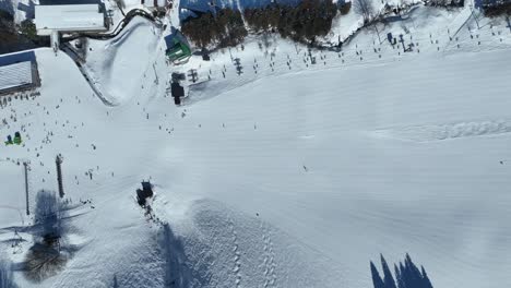 High-altitude-shot-of-bottom-of-ski-run,-static-shot-of-skiers-arriving-at-base-of-mountain-lining-up-for-the-chairlifts
