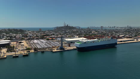 Drone-flying-around-a-bulk-carrier-at-the-industrial-Port-of-Mazatlan,-sunny-Mexico