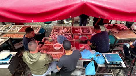 Men-working-in-open-air-fish-market-under-the-red-trap,-static-from-behind
