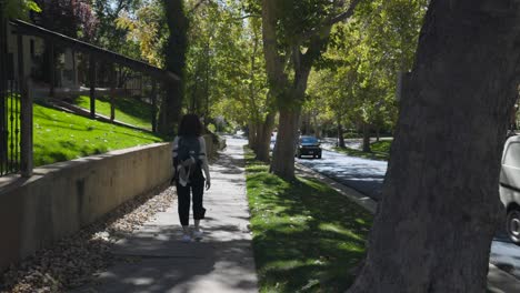 Frau-Mit-Rucksack-Geht-Auf-Bürgersteig-Im-Schatten-Von-Bäumen,-Salt-Lake-City,-Utah,-Usa