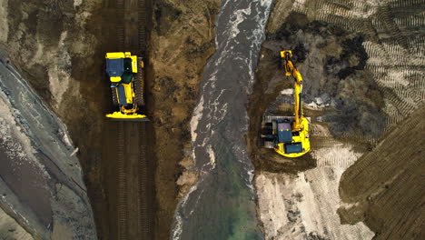Aerial-top-down-shot-bulldozer-retreating-in-new-found-land-and-excavator-removing-sediment-from-a-water-canal