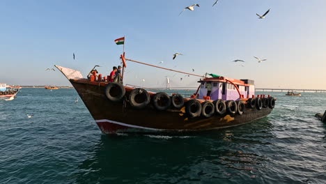 Una-Escena-Pintoresca-Se-Desarrolla-Cuando-Un-Barco-De-Madera,-Adornado-Con-La-Bandera-De-La-India,-Zarpa-Del-Puerto,-Acompañado-Por-Pescadores-Cercanos,-Simbolizando-Una-Mezcla-De-Patriotismo-Y-Medios-De-Vida-Costeros.