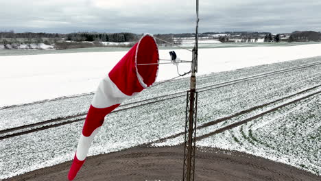 A-revealing-shot-of-a-red-and-white-windsock-on-a-small-snow-covered-airfield,-captured-in-the-northern-part-of-Denmark