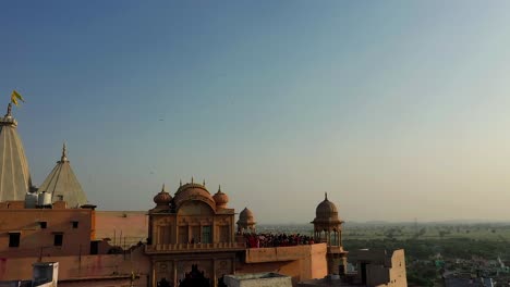 camera-going-up-from-the-roof-of-the-temple-where-many-people-are-playing-color-and-people-from-the-temple-are-going-to-do-darshan-and-going-outside-and-the-vehicle-is-shown