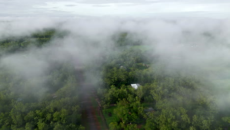 Aerial-Drone-of-Misty-Tendrils-of-Cloud-Fog-Above-Rural-Estate-and-Dirt-Road