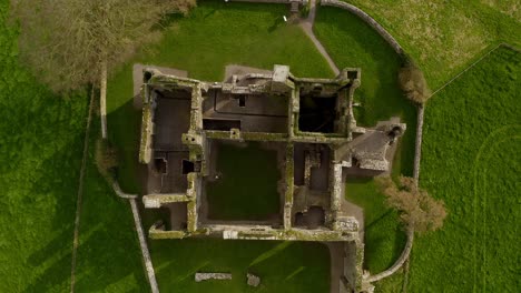 Aerial-top-down-descends-on-Bective-Abbey-walls-on-sunny-green-Irish-day,-drone-overview