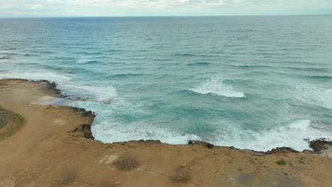 Turquoise-blue-ocean-water-waves-crash-on-rocky-arid-red-cliff-beach-in-Cyprus