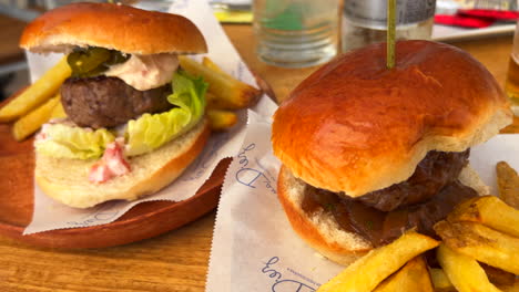 Two-delicious-juicy-burgers-with-french-fries-on-wooden-plates-at-a-restaurant-in-Estepona-Spain,-4K-shot