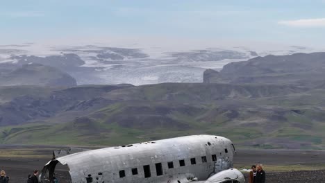 Aerial-View-of-Abandoned-Airplane-on-Coast-of-Iceland-With-Glacier-Ice-Cap-on-Hills-in-Background-60fps