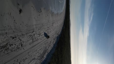 Aerial-footage-of-a-jeep-driving-over-the-sandy-beach-of-Wylie-bay-rock