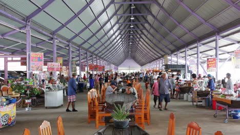 Bei-Einem-Spaziergang-Durch-Einen-Lokalen-Lebensmittelmarkt-Essen-Die-Bewohner-Von-Bangkok,-Während-Andere-In-Einem-Gebäude-In-Bangkok,-Thailand,-Noch-Immer-Nach-Nahrungsmitteln-Suchen,-Die-Sie-Kaufen-Und-Essen-Können