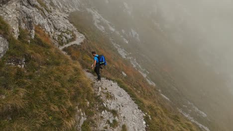 Aerial-View-Of-Male-Hiking-Along-Mountain-Path-In-Lecco-Alps-With-Foggy-Misty-Air-In-Background