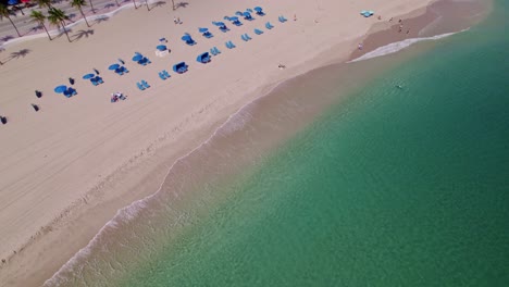 Elegant-visual-aerial-drone-shot-of-beach-and-sand-with-calm-waters-blue-water-blue-sky-palm-trees-ft