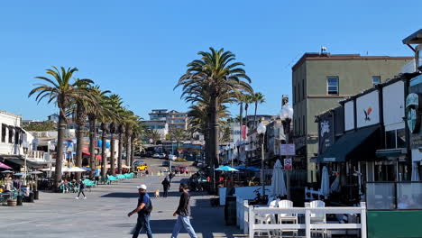 People-walk-around-Manhattan-beach-california-USA-town-stores-palm-trees-slow-motion-skyline-background-in-daylight-sunny-weather