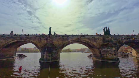 Puente-De-Carlos-Con-Esculturas-De-Un-Barco-Que-Navega-Por-El-Río-Moldava-En-Praga,-República-Checa