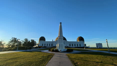 Architectural-landmark-of-los-angeles-California-people-walk-in-urban-park-with-shiny-morning-skyline,-Grass-pathwalk-to-white-monument