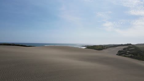 Cinematic-view-across-natural-landscape-of-sand-dunes-leading-to-ocean-waves-crashing-onto-the-paradise-beach-shore