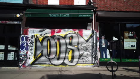 Wide-shot-of-a-man-with-a-walker-passing-by-a-shuttered-store-in-Kensington-Market