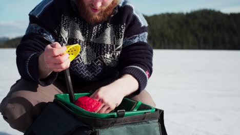 Man-Looking-For-Something-On-Its-Tackle-Bag-With-Small-Fishing-Rod-And-Ice-Fishing-Scooper