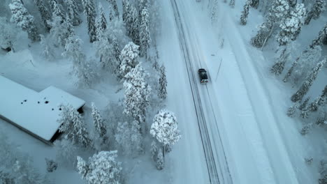 Eine-Drohne-Fängt-Einen-Schwarzen-Lieferwagen-Ein,-Der-Auf-Einer-Verschneiten-Straße-In-Der-Nähe-Des-Polarkreises-In-Luosto,-Finnland,-Fährt-Und-Bietet-Eine-Atemberaubende-Luftaufnahme