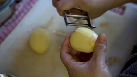 En-Cámara-Lenta,-Una-Persona-Pela-Una-Papa,-Simbolizando-El-Proceso-De-Preparación-De-Alimentos,-Preparación-De-Vegetales-Para-Cocinar-Y-La-Promoción-De-Una-Dieta-Vegetariana-Y-Hábitos-Alimentarios-Saludables.