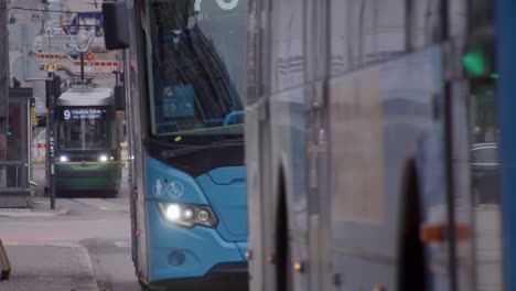 Public-transport-buses-drive-past-camera-on-city-street,-Helsinki-FIN