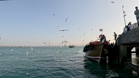 The-cinematic-shot-captures-the-essence-of-wooden-boat-with-India's-flag,-docked-on-the-pier,-with-passengers-debarking-and-embarking,-blending-cultural-symbolism-with-coastal-life-in-motion