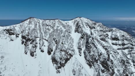 Aerial-shot-push-in-over-top-of-Myoko-Mountain-Summit,-Japans-coast-line-and-ocean-sea-visible-in-background