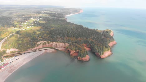 Very-high-aerial-shot-of-a-peninsula-surrounded-by-tress,-a-beach,-and-super-clear-water-in-New-Brunswick