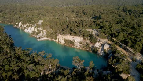 Backward-drone-shot-of-turquoise-little-lake-in-between-a-dense-forest-in-Tasmania,-Australia