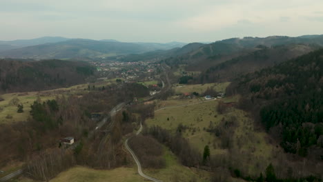 A-scenic-aerial-view-of-Jedlina-Zdrój,-showcasing-the-town's-nestled-position-within-a-verdant-valley-flanked-by-rolling-forested-hills