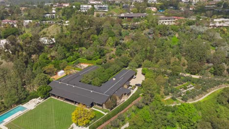 Toma-Aérea-Alejándose-De-Un-Enorme-Complejo-De-Casas-Y-Propiedades-En-Beverly-Hills,-Mansión-En-Forma-De-U-En-Una-Colina-Aislada-Arbolada-Vista-Desde-Arriba