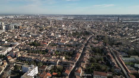 Rue-de-Pessac-and-City-center-with-basilica-and-Garonne-river-in-the-distance-Bordeaux-France,-Aerial-pan-left-shot